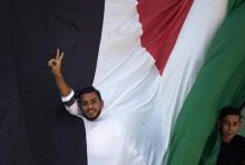 Un Palestinien fait le signe de la victoire sur fond d'un drapeau palestinien à Beit Hanun, dans la 