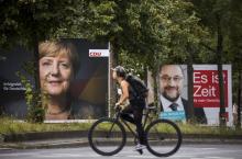 Un cycliste passe devant les affiches de campagne de la chancelière allemande Angela Merkel et du ch