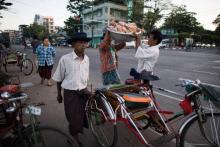 Un conducteur de rickshaw aide sa cliente qu'il vient de conduire près d'un marché de Rangoun à replacer sur sa tête une bassine pleine de poulets, le 3 décembre 2017