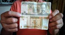 Un ouvrier cubain montre 1 CUP (peso cubain) et 1 CUC (peso cubain convertible) à la Havane le 8 février 2018. Cuba va tenter cette année d'unifier sa monnaie et le taux de change