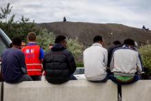 Des migrants attendent aux côtés d'un employé de l'Office français de l'immigration et de l'intégration le 16 août 2017 à Calais