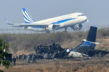 An airplane taxis at the international airport in Kathmandu on March 13, 2018, near the wreckage of a US-Bangla Airlines plane that crashed on March 12.At least 49 people were killed and 22 injured wh