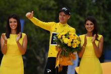Le vainqueur du Tour de France 2017 Chris Froome entouré de deux hôtesses sur les Champs-Élysées, à Paris, le 23 juillet 2017