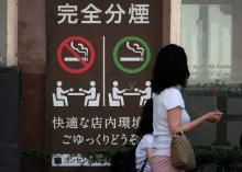 Une femme et sa fille passe devant un café affichant des "zones séparées" pour les fumeurs et les non-fumeurs à Tokyo, le 27 juin 2018