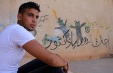Le Syrien Mouawiya Sayassina, qui a commencé à faire des graffitis anti-régime en 2011, est assis à côté d'un mur où est écrit en arabe "A ton tour docteur", dans un quartier rebelle de la ville de De