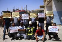 Des secouristes membres des Casques blancs exhibent des pancartes demandant à la communauté internationle de les aider à être évacuer du sud syrien, dans la ville de Deraa, le 24 juillet 2018