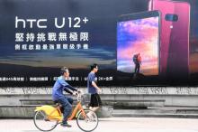 Des cyclistes passent devant une publicité murale du fabricant de smartphones HTC à Tapei, le 3 juillet 2018 Le groupe va supprimer 1.500 emplois, soit un cinquième de ses effectifs