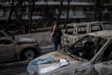Un femme se tient au milieu de voitures calcinées le 25 juillet 2018 après un incendie de forêt qui a ravagé la petite ville grecque de Mati