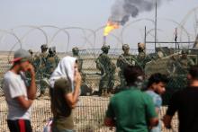 Des jeunes irakiens manifestent devant l'entrée d'un champ pétrolier gardé par des soldats, le 14 juillet 2018 à Al-Qournah, dans la province de Bassora (sud)
