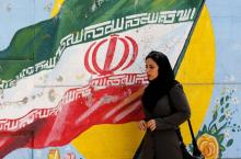 Une Iranienne marche devant le drapeau national peint sur un mur de Téhéran le 6 août 2018