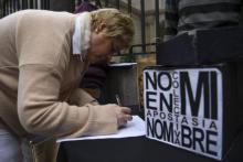 Une femme paraphant un document renonçant à son baptême à côté d'une pancarte disant "Pas en mon nom. Apostasie collective", devant le siège de la conférence épiscopale argentine le 24 août 2018