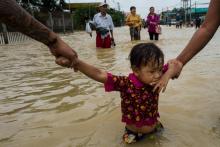 Des habitants tiennent par la main un enfant qui marche dans les rues inondées de la région de Bago, à 68 km de Rangoun, le 29 juillet 2018