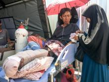 Blessé dans le séisme meurtrier en Indonésie, Alimuddin (G) allongé sur un lit de fortune patiente avec son épouse Maria Ulfa (D) devant un hôpital de Mataram sur l'île de Lombok, le 6 août 2018