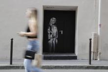Une femme passe devant le pochoir de l'artiste Bansky le 25 juin 2018, dans une rue près de la salle de concert du Bataclan