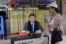 Une femme passe avec son bébé à Nouveau Taipei le 2 janvier 2019 devant une télévision montrant le président chinois Xi Jinping qui prononce un discours intransigeant envers Taïwan