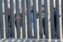 Des candidats à l'immigration aux Etats-Unis, venus du Honduras, regardent à travers le mur frontalier à San Ysidro (Californie)