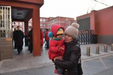 Une femme portant son enfant passe devant le portail d'une école primaire où un homme a attaqué des enfants dont vingt ont été blessés, à Pékin le 8 janvier
