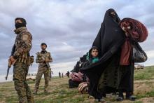 Une femme et son enfant passent devant des membres des Forces démocratiques syriennes, après avoir fui le dernier réduit du groupe Etat islamique à Baghouz, en Syrie, le 28 février 2019