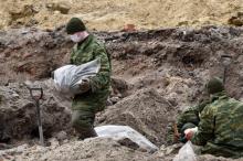 Des hommes en treillis remplissent de grands sacs plastiques d'ossements après la découverte d'une fosse commune sur le site d'un ancien ghetto juif, le 27 février 2019 à Brest, au Belarus