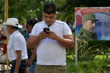 Un homme utilse son téléphone portable dans les rue de La Havane avec un portrait de Fidel Castro en fond, le 17 mars 2019