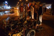 Des Irakiens devant la carcasse d'une voiture piégée qui a explosé le 8 mars 2019 à Mossoul tuant deux personnes