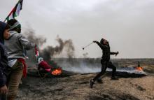 Un Palestinien lance une pierre en direction des soldats israéliens postés de l'autre côté de la barrière frontalière entre la bande de Gaza et Israël, lors du premier anniversaire des "Grandes marche