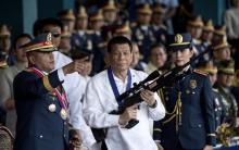 Le président philippin Rodrigo Duterte armé d'un fusil de sniper lors d'une cérémonie de passation de pouvoir à Manille le 19 avril 2018. A gauche, l'ancien chef de la police Ronald dela Rosa qui devr