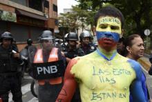 Des partisans de l'opposition vénézuélienne, comme cet homme au corps peint aux couleurs du drapeau national, manifestent devant les forces anti-émeute près de la base militaire de La Carlota, à Carac