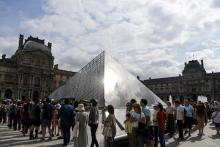 Des touristes font la queue devant la pyramide du Louvre pour entrer au musée du Louvre le 19 juillet 2019 à Paris