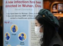 Une femme, un masque de protection sur le visage, passe devant un panneau d'information sur le nouveau coronavirus détecté en Chine, lors de son arrivée à l'aéroport de Londres, le 28 janvier 2020