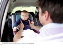 Une homme installe un bébé dans un siège auto.