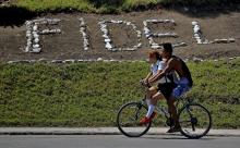 Des cyclistes passent devant un terre plein où est inscrit le nom de l'ancien chef d'État Fidel Cast