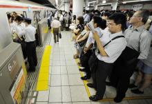 Des passagers attendent de pouvoir entrer dans un métro, pendant l'heure de pointe à Tokyo, le 12 ju