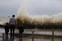 Un homme et des enfants regardent des vagues s'écraser contre un mur, le 4 janvier 2018 à Asnelles