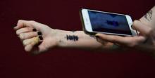 Hanna Washlake scanne avec son téléphone l'onde sonore qu'elle vient de se faire tatouer sur le poignet: "Salut Hanna, c'est Maman. Je suis si fière de toi", le 12 avril au Black Raven Tattoo à Torran