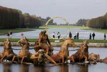 Des visiteurs marchent dans les jardins de Versailles, passant devant une sculpture de l'artiste sui