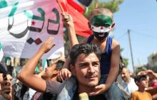 Un homme porte un enfant dont le visage est peint aux couleurs du drapeau de la révolution syrienne, lors d'une manifestation pour la libération des détenus aux mains du régime de Damas, à Maaret al-N