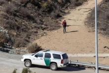 Un hombre con un niño en brazos camina hacia una patrulla estadounidense tras cruzar ilegalmente la frontera, visto desde la mexicana Tijuana