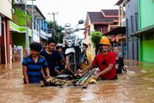 Des personnes affectées par les inondations transportent un scooter sur un radeau de fortune le 23 janvier 2019 à Makassar