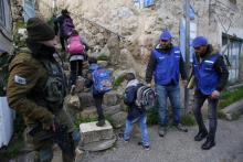 Un soldat israélien (L) présent alors que des membres de l'organisation palestinienne "Jeunes contre les colonies" accompagnent le 10 février 2019 des enfants à l'école à Hébron, en Cisjordanie occupé