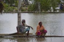 Un couple assis sur un tronc d'arbre près de leur maison encerclée par les eaux à Khulna (Bangladesh), le 4 mai 2019, après l'arrivée du cyclone Fani, dont l'intensité a fortement faibli