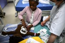 La petite Nyobe apprend à changer un cathéter sur une poupée avec l'aide d'une infirmière dans le service de concérologie pédiatrique de l'Hôpital Armand-Trousseau, le 16 mars 2021 à Paris