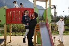 Le président Emmanuel Macron porte une enfant dans ses bras lors d'une visite dans un centre de dépistage et de suivi pour autistes, le 2 avril 2021 à l'hôpital de Saint-Egrève, près de Grenoble