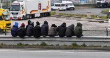 Des migrants sont assis sur une barrière près de la rocade du port de Calais le 30 mars 2018