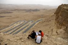 Des touristes assis au bord du "cratère" de Ramon, dans le désert du Néguev en Israël, le 6 mai 2018