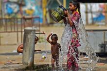 Une femme et des enfants se rafraichissent avec l'eau d'un robinet public lors d'une chaude journée d'été, le 28 avril 2022 à Allahabad, en Inde